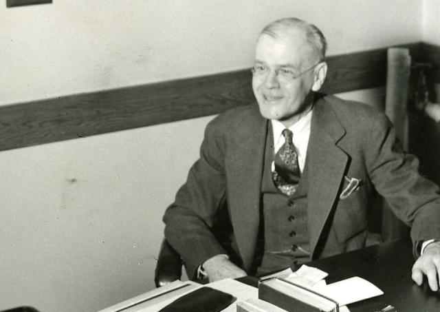 A black-and-white photo of Edward S. "Beanie" Drake seated at his desk.