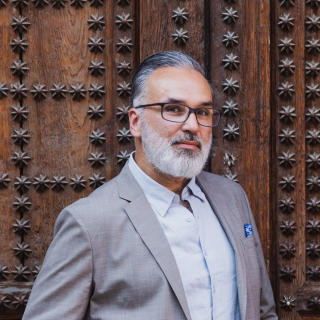 Photo of a latino man with grey hair wearing a suit